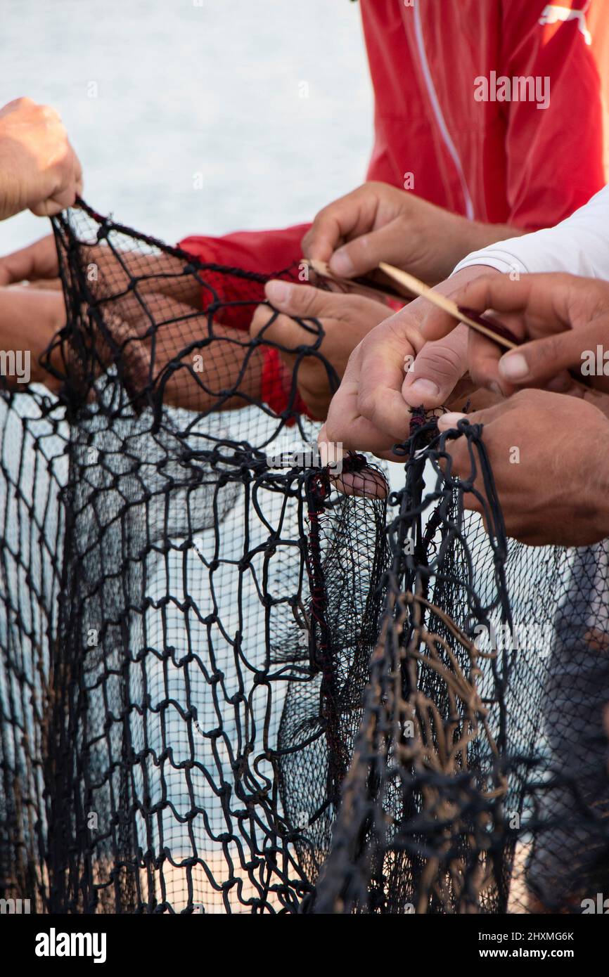 Tribunj, Croatia- August 23, 2021: Fishermen repairing the fishing net , working hand with wooden needle close up detail Stock Photo