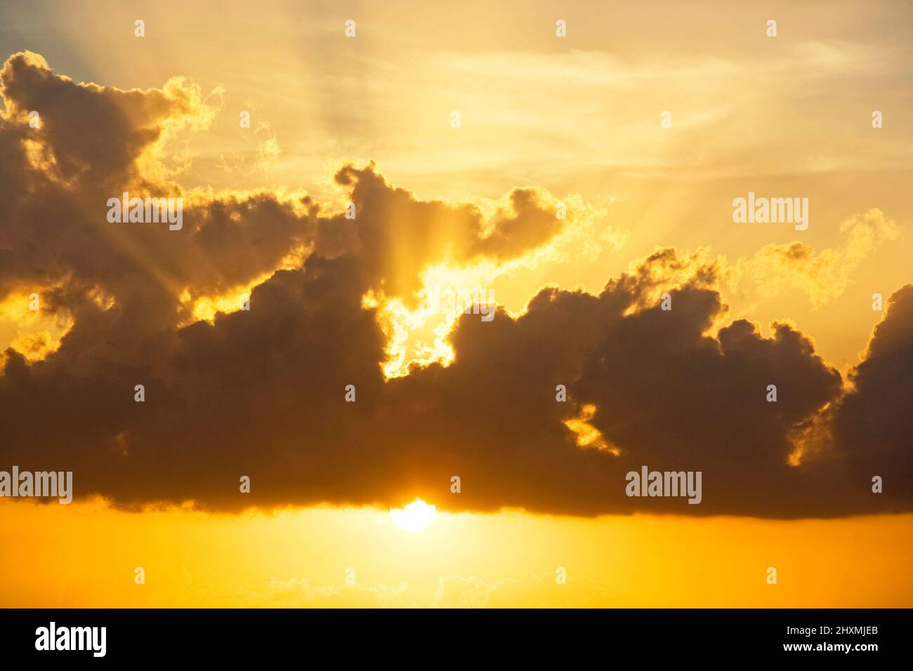 SUN PEAKING BELOW CLOUDS WITH ON ORANGE SKY Stock Photo