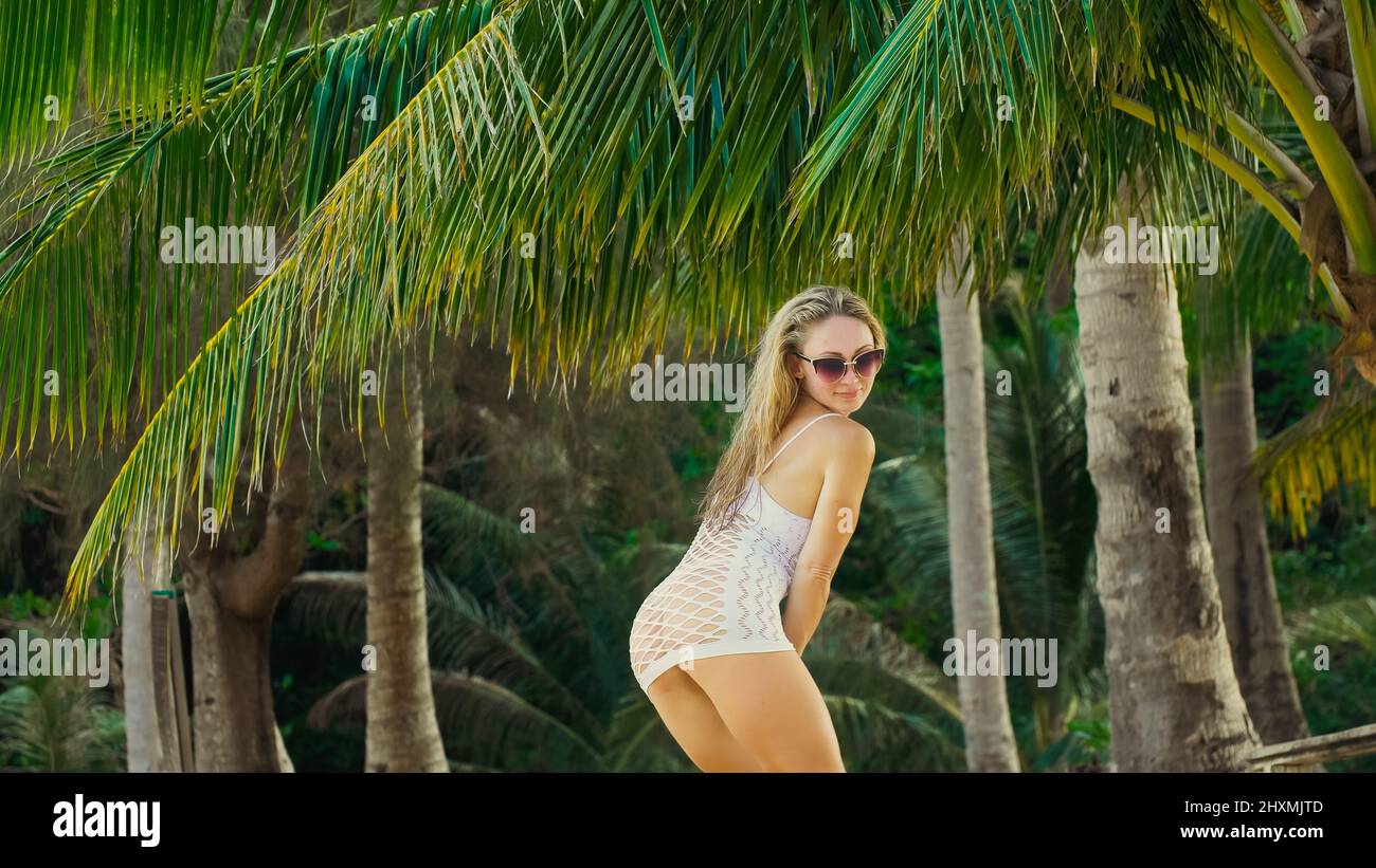 Sexy vibrant young lady dancing on the beach near the sea. The sunburnt woman tourist spends her vacation. Exciting Brazilian dancing of the buttocks. Stock Photo