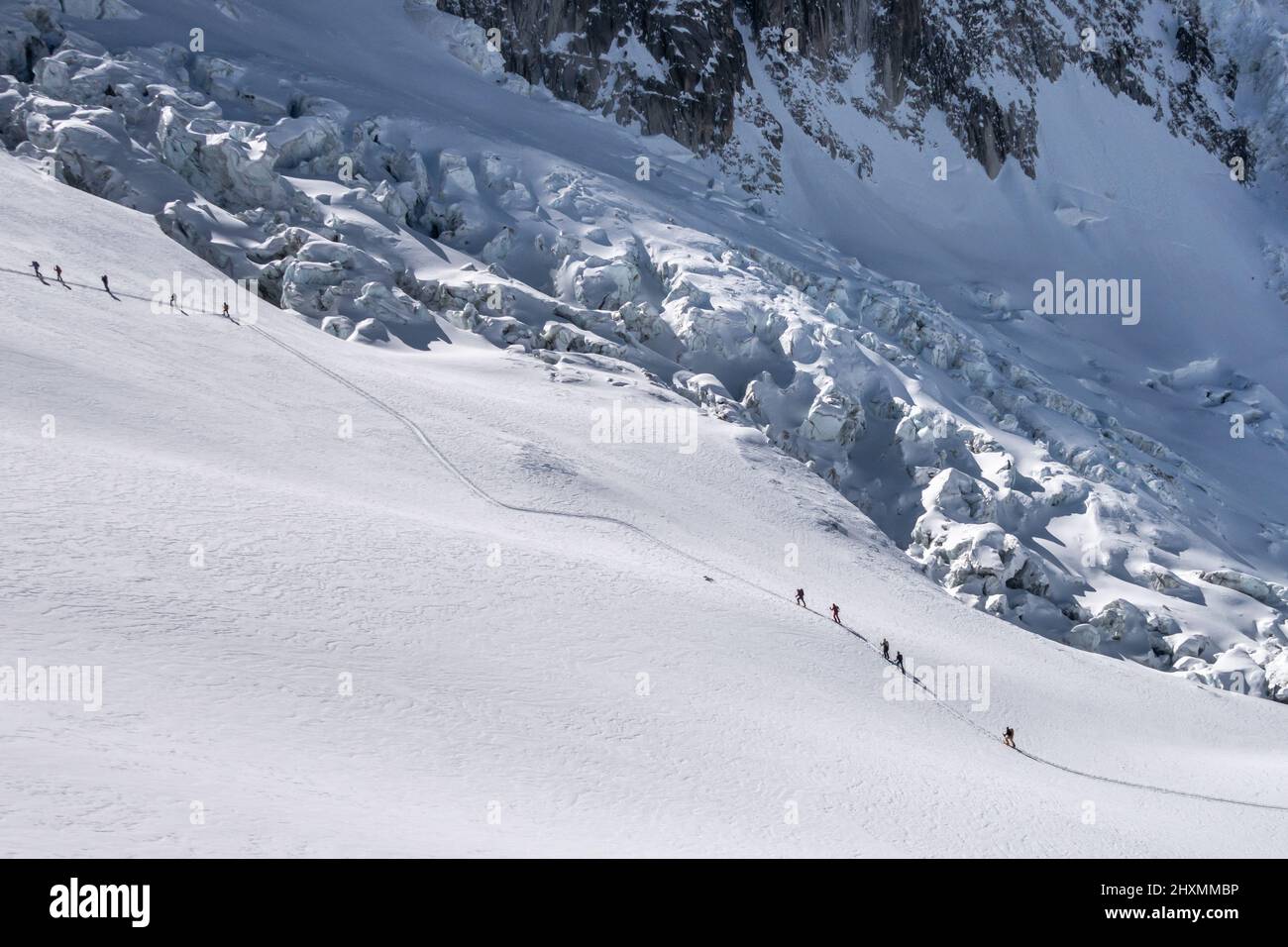 Two groups of skiers touring up a track along the Periades glacier towards the Periades range of mountain peaks above the Vallee Blanche with numerous Stock Photo