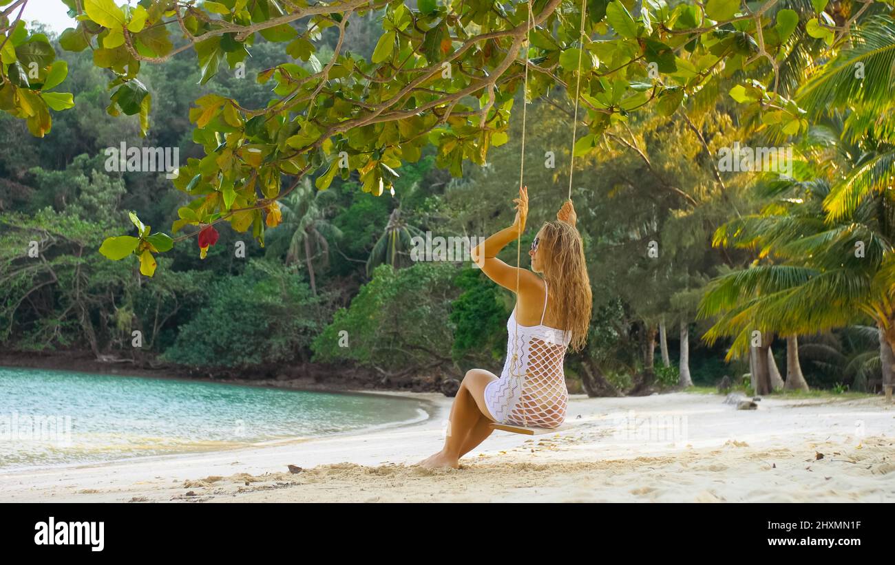 Sexy hot woman is swinging on a swing. Erotic bad girl posing on the beach against the backdrop of the sea. Concept natural beauty body, femininity an Stock Photo