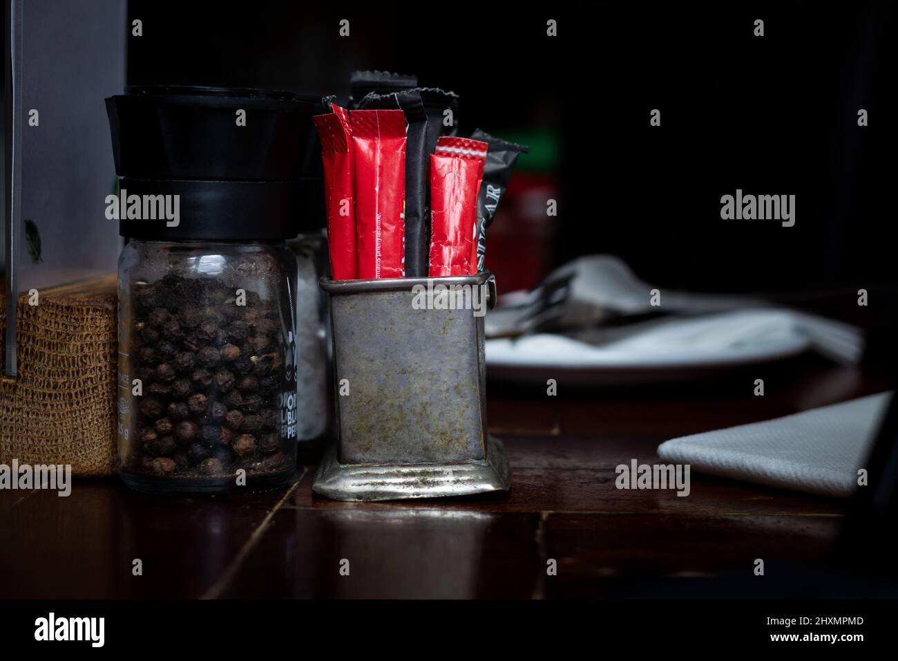 Rustic metal sugar sachet and sweetner container. Restaurant table with black pepper Stock Photo