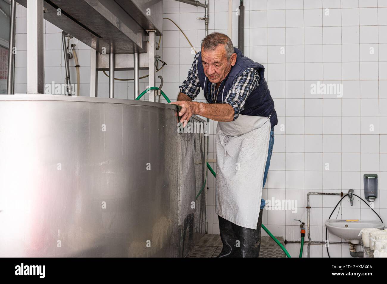 old man in an apron scrubbing the outside of stainless steel container Stock Photo