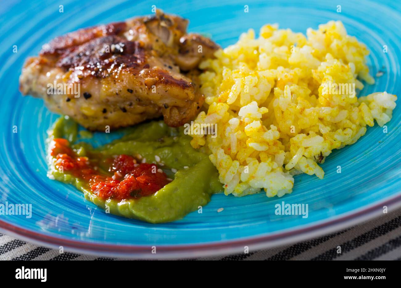 Baked chicken thighs and spicy rice with sauces Stock Photo - Alamy