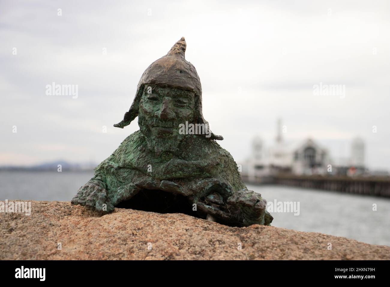 Bronze statue of a fictitious character looking over the top of a large rock Stock Photo
