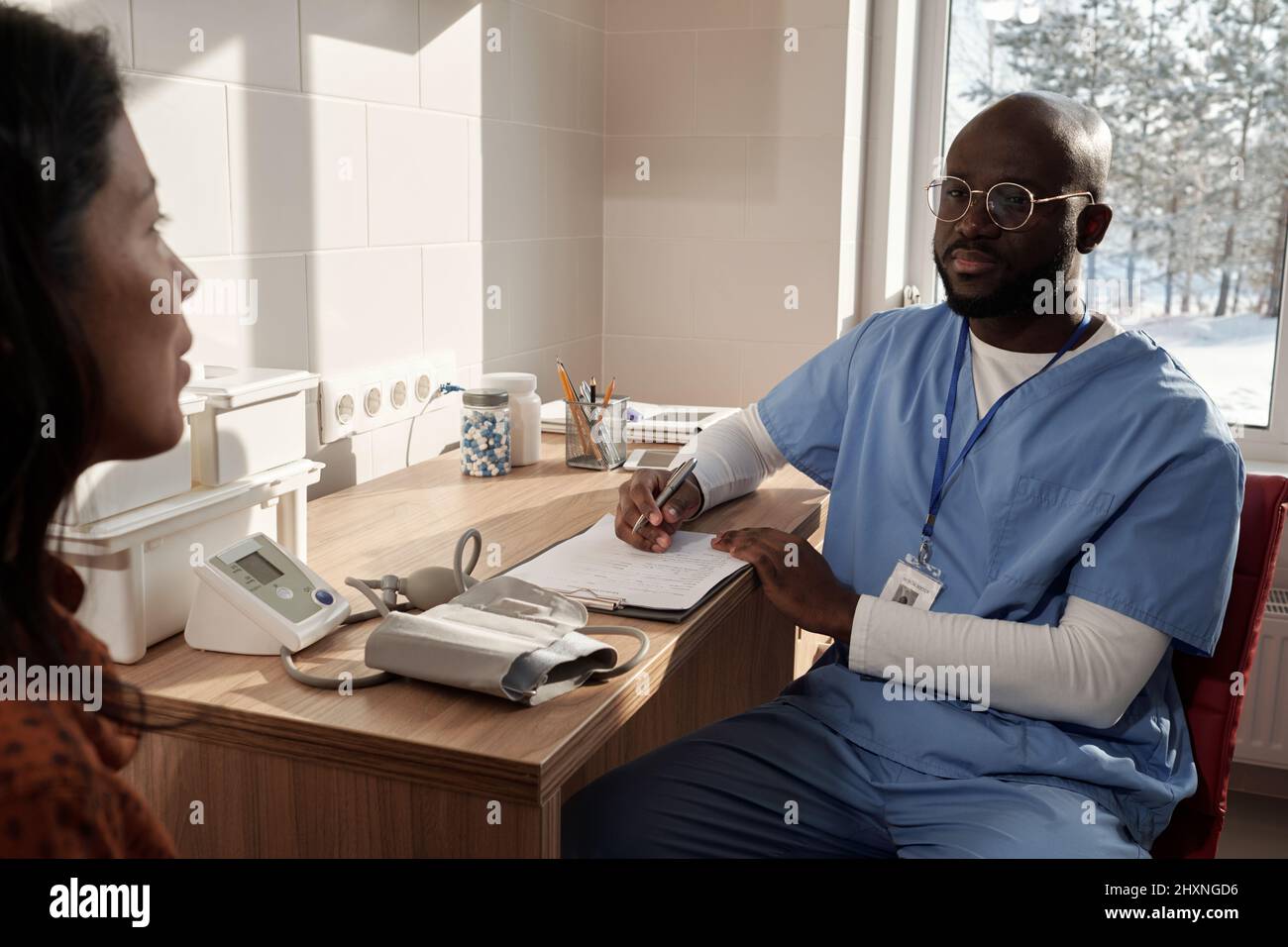 Young serious doctor in uniform listening to female describing her