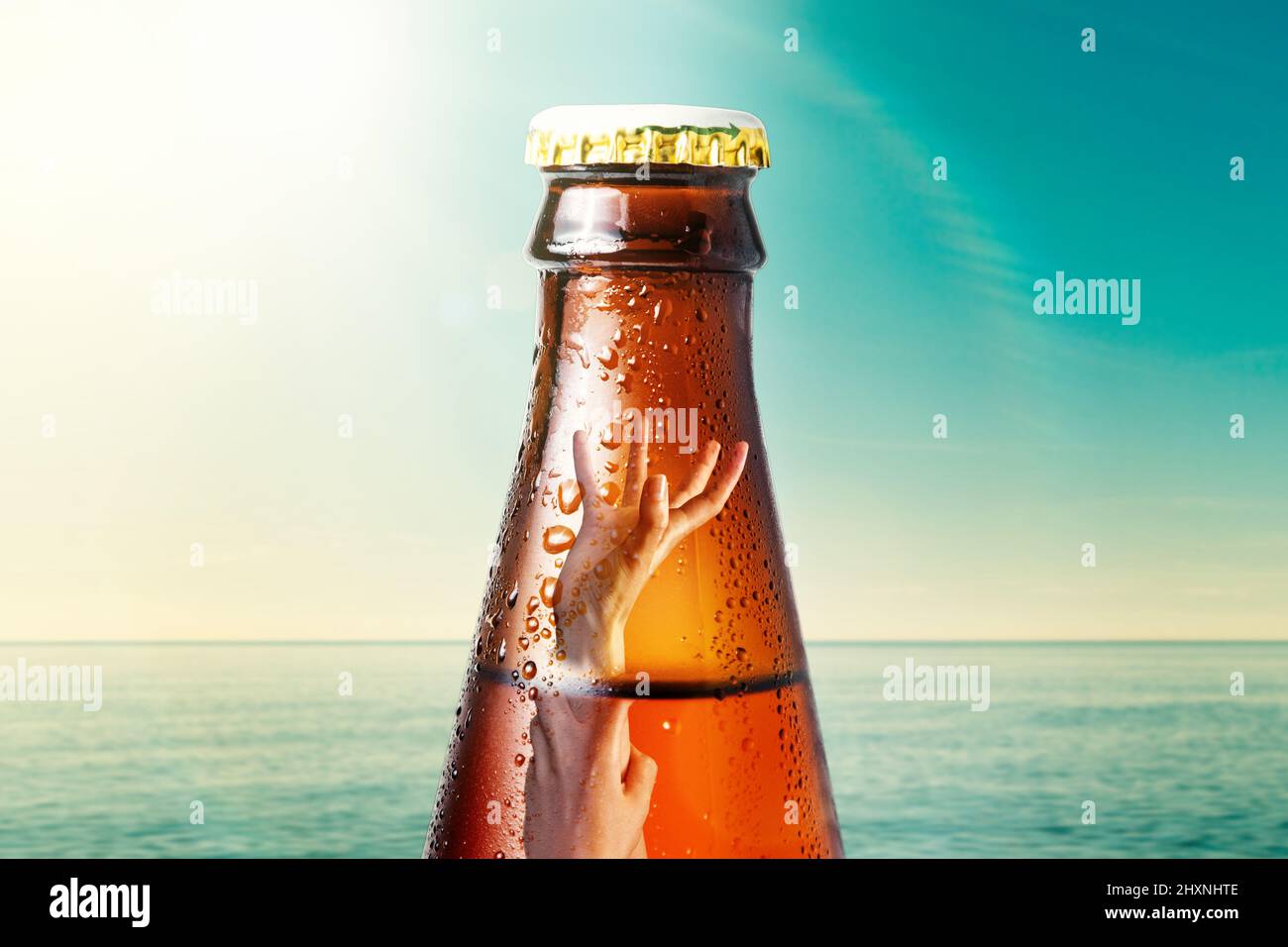 Close-up of the neck of wet glass bottle of dark beer against the background of the ocean and the sky. Inside it drowning hand. Alcoholic beverages on Stock Photo
