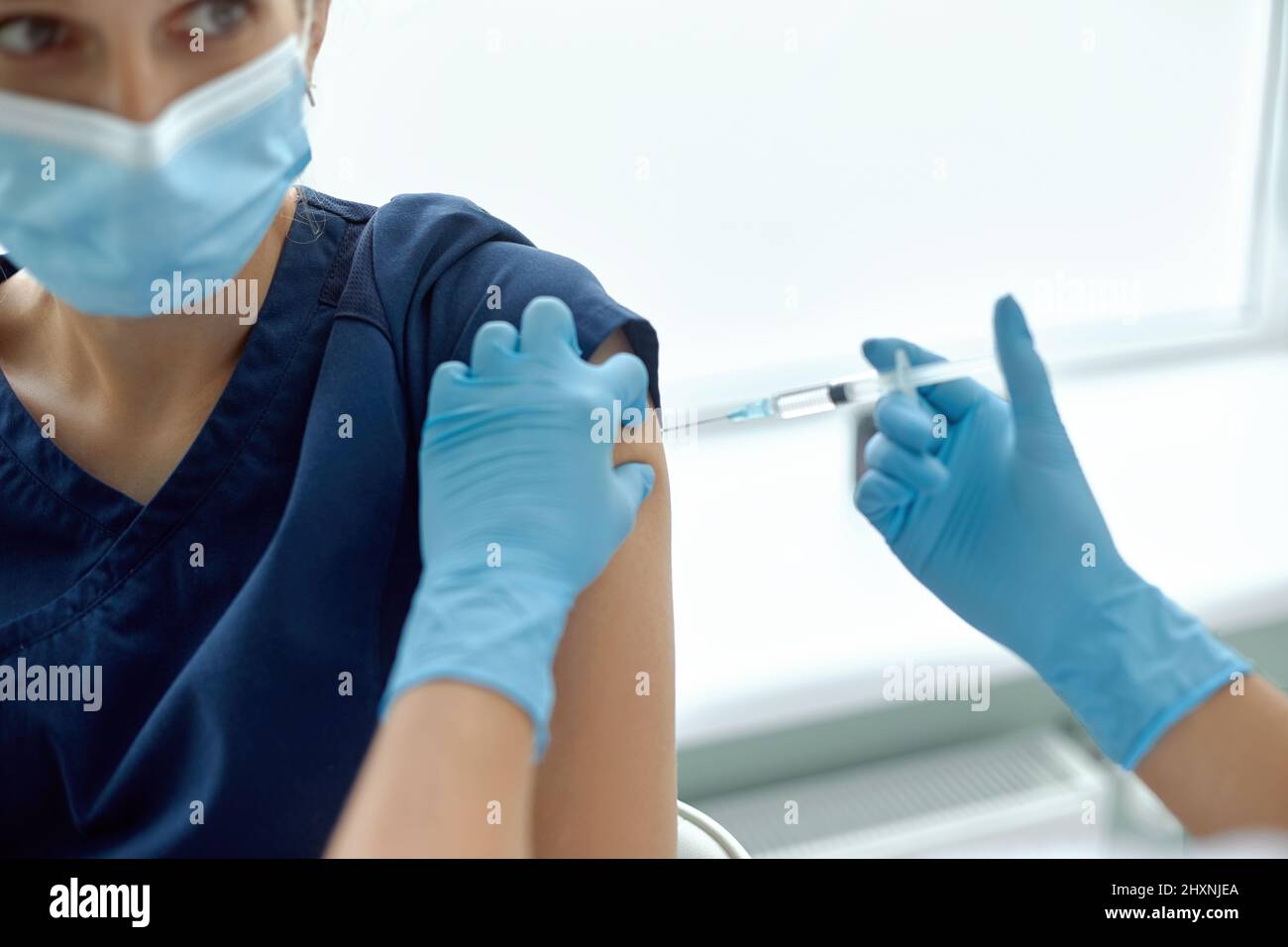 Woman in medical face mask getting injection at hospital. Doctor or nurse preparing syringe to give shot to female patient Stock Photo