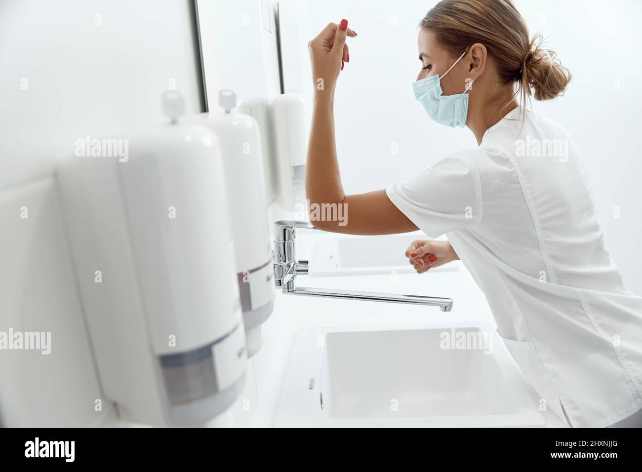 woman closes the water tap with her elbow Stock Photo