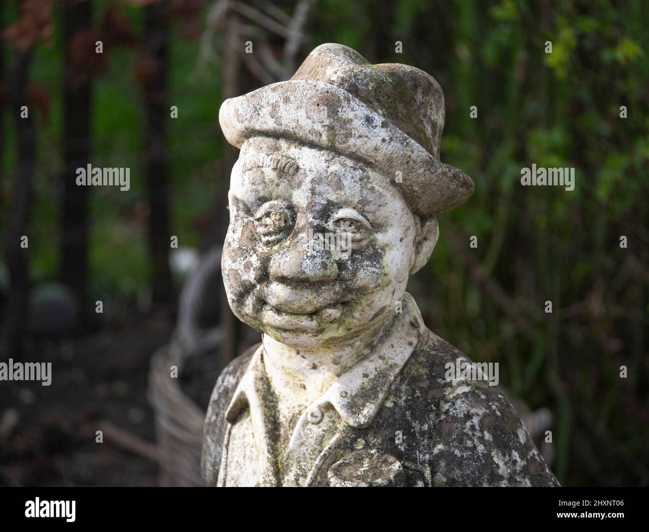 Close up photo of a hard weathered concrete statue, man in suit with hat Stock Photo