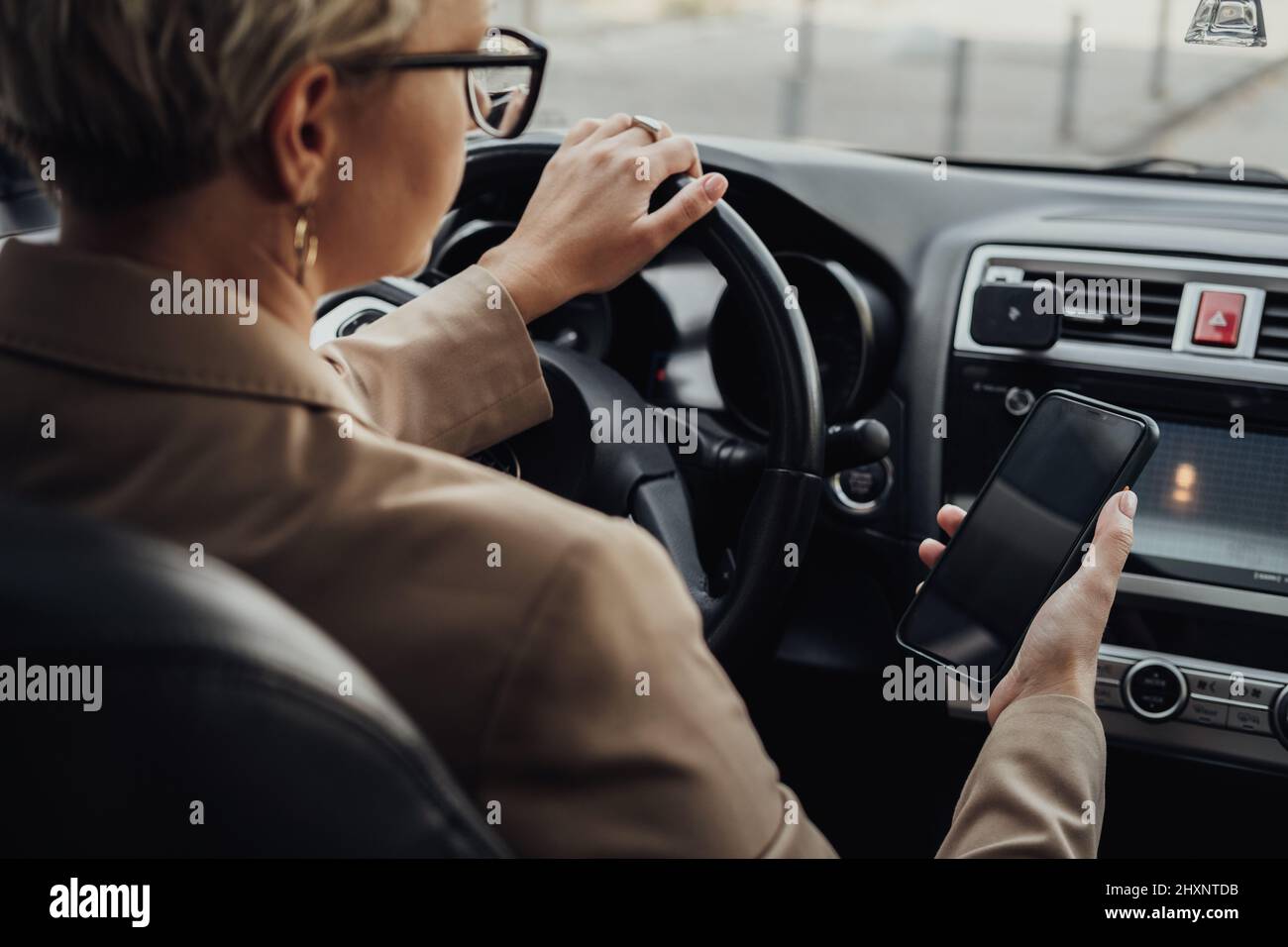 Business Woman Using a Smartphone While Driving Car, View from Back Seat Stock Photo