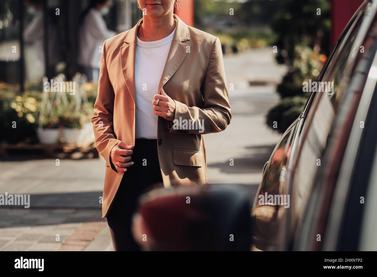 Unrecognisable Stylish Woman in Brown Jacket Moving Near the Car Stock Photo