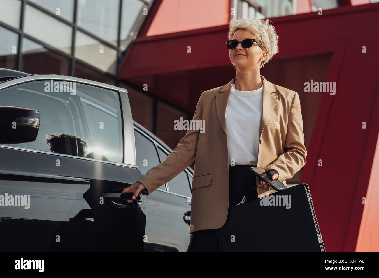 Elegant Female Entrepreneur with Briefcase in Hand Opening Door of the Luxury Car Stock Photo