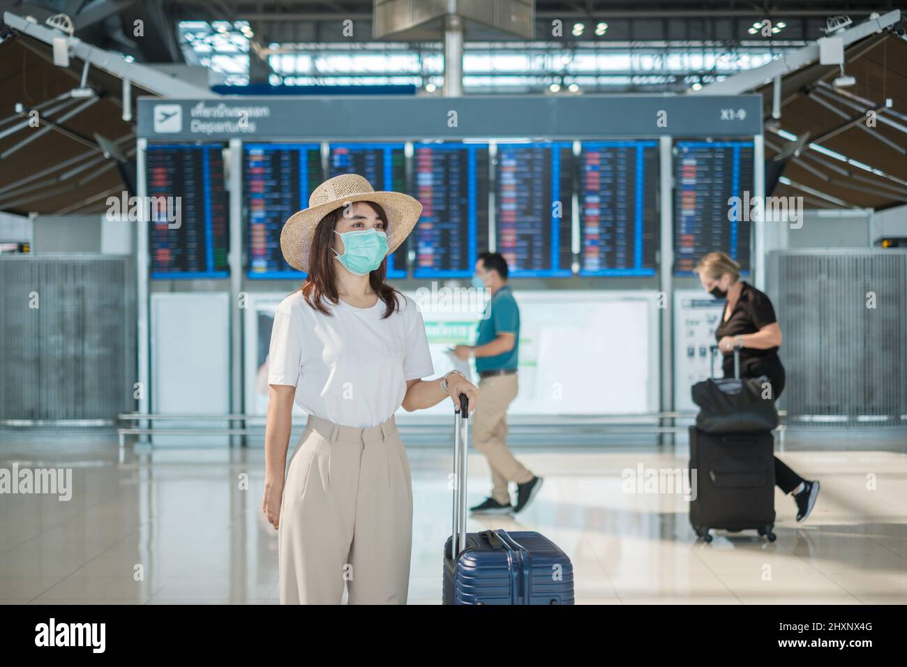 Young female wearing face mask with luggage walking in airport, protection Coronavirus disease infection, Asian woman traveler with hat. Time to trave Stock Photo