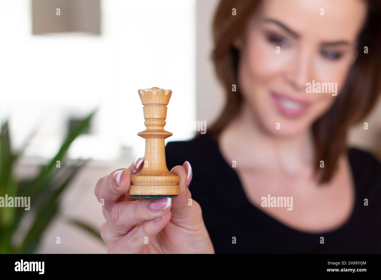 Confident young woman holding chess queen, depth of field Stock Photo