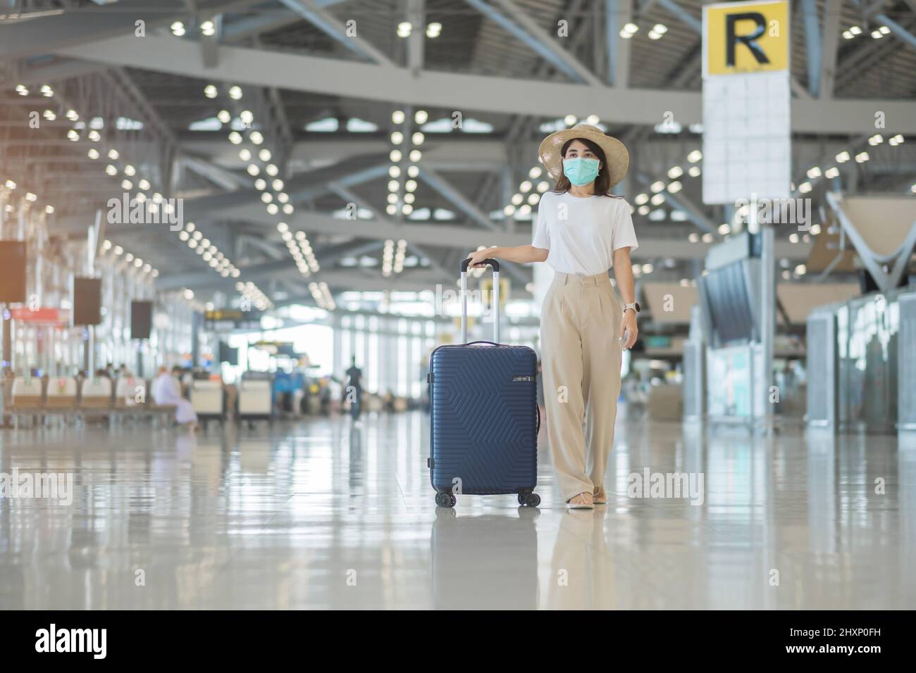 Young female wearing face mask with luggage walking in airport, protection Coronavirus disease infection, Asian woman traveler with hat. Time to trave Stock Photo
