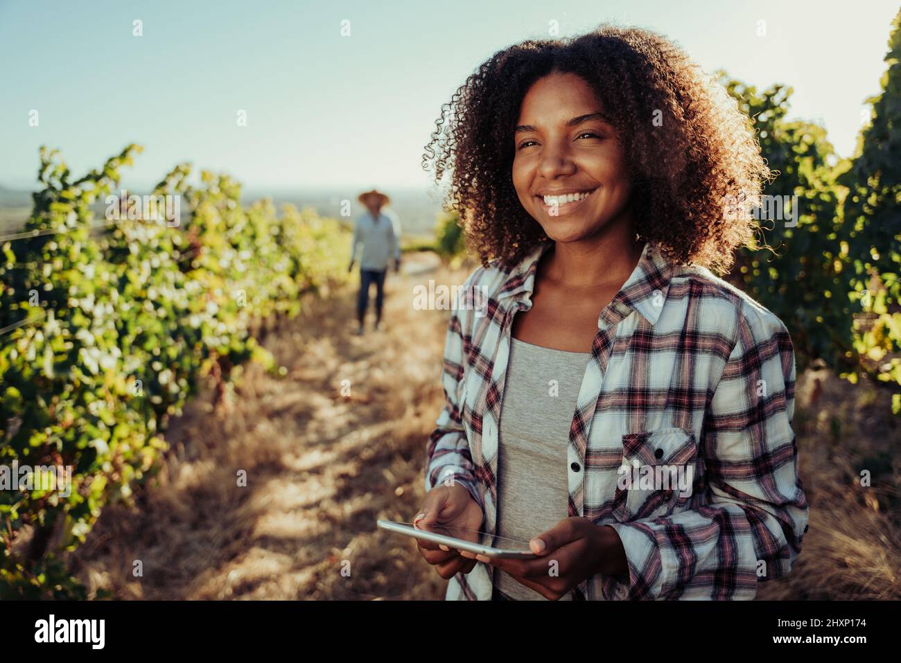 Mixed race female smiling while holding digital tablet working in vineyards with male colleague Stock Photo