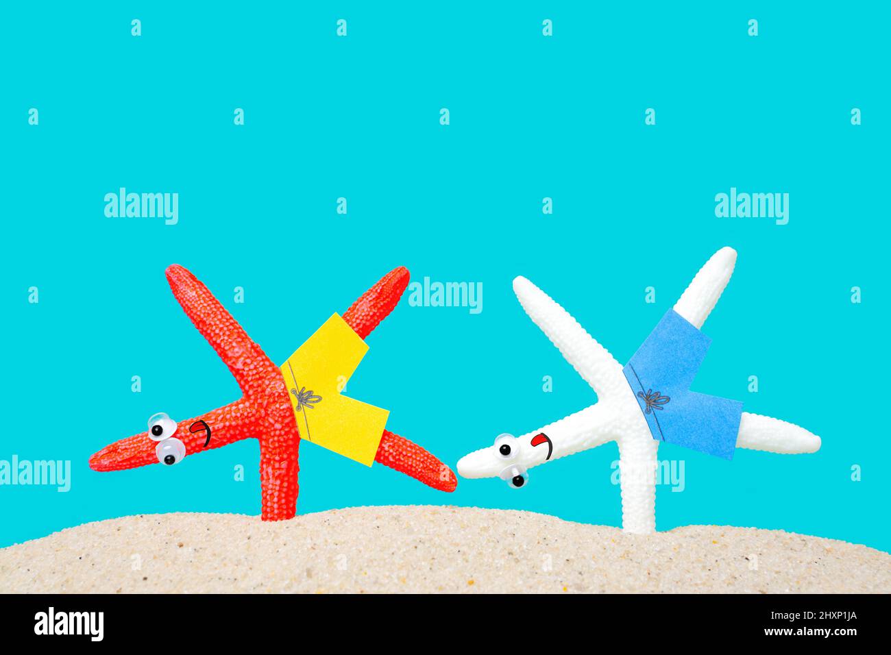 Two starfish characters making the one arm handstand on a sandy beach. Morning seaside yoga session. Stock Photo