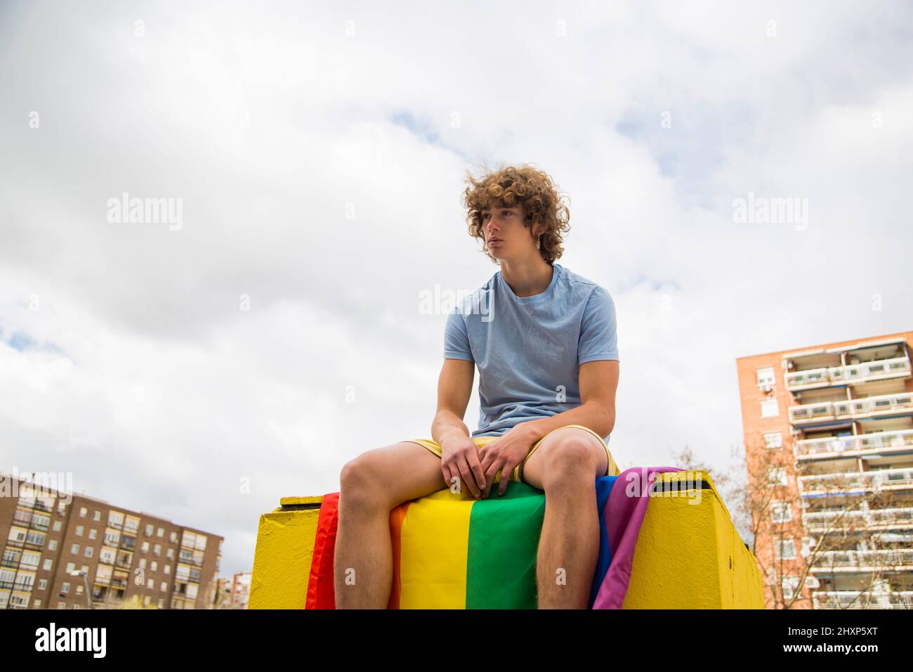 young gay man posing sitting on a gay pride flag Stock Photo