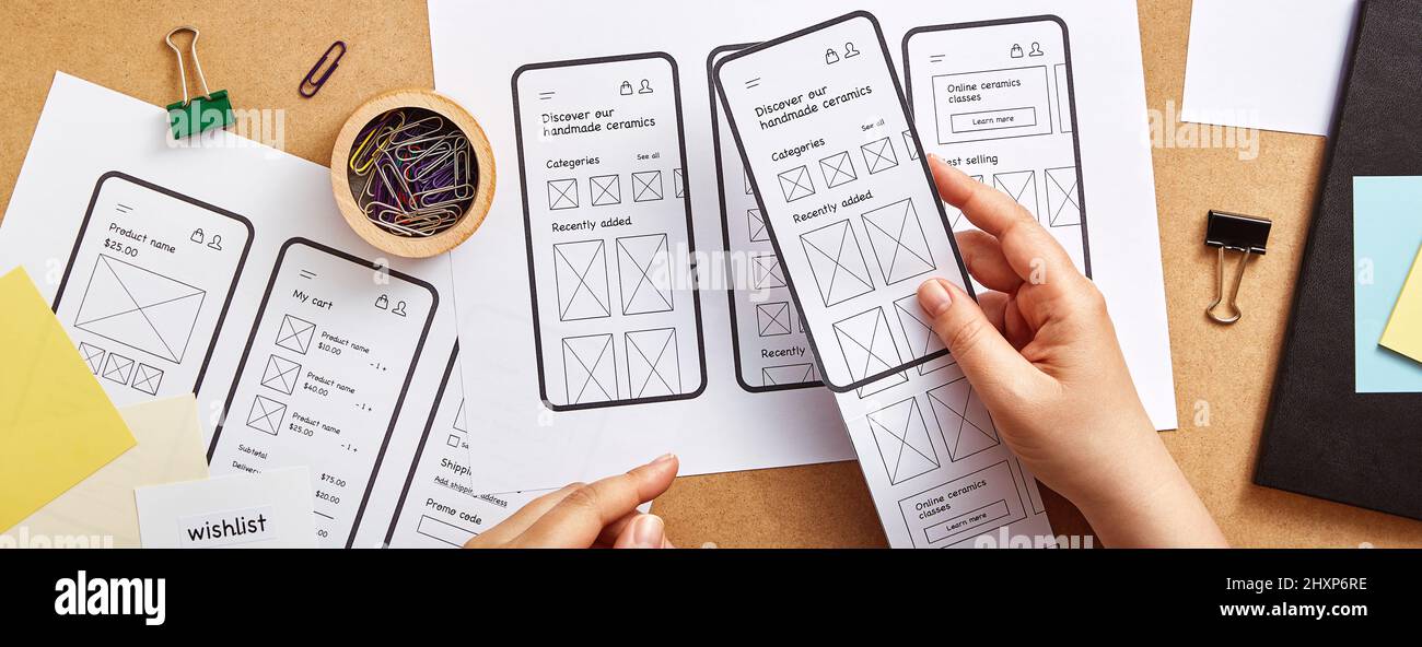 Web product designer working on mobile responsive website concept banner. Flat lay image of several app wireframe sketches over product designer desk. Stock Photo