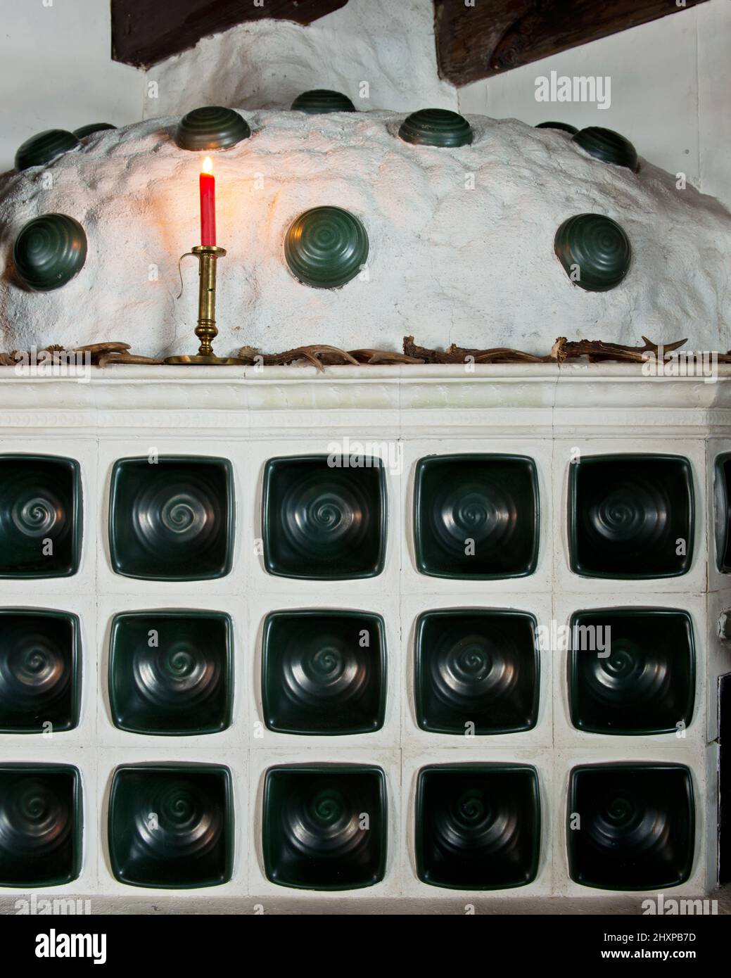 detail of massive green tiled stove with red candle and antlers Stock