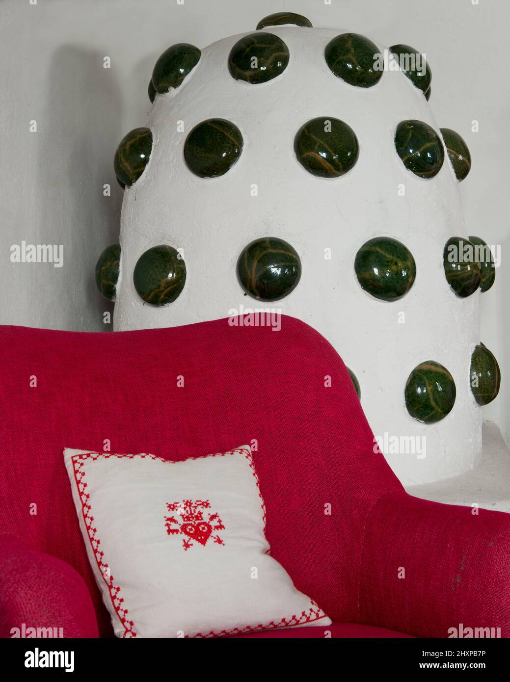 detail of Alpine style bedroom with tiled stove in white and green, red chair and white embroidered cushion Stock Photo
