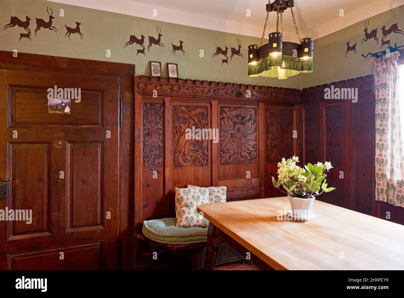 carved wooden paneling in country kitchen with wooden dining table, green wall with deer painting and metal historistic lamp Stock Photo