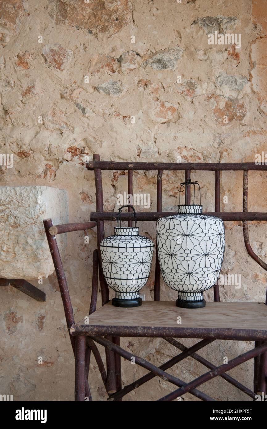 two white chinese lampions with filigran black decoration on a wooden bench in front of an old stone wall Stock Photo