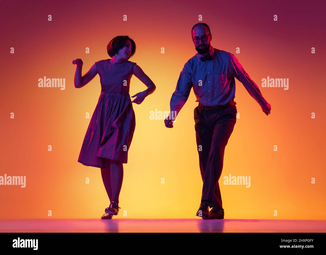 Portrait of excited man and woman, couple of dancers in vintage retro style outfits dancing lindy hop dance isolated on gradient yellow and purple Stock Photo