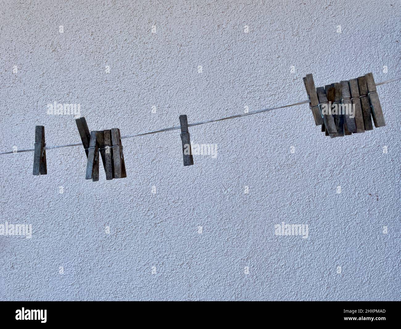 Old wooden clothes pins hanging on clothes line against white wall. Selective focus. High quality photo Stock Photo