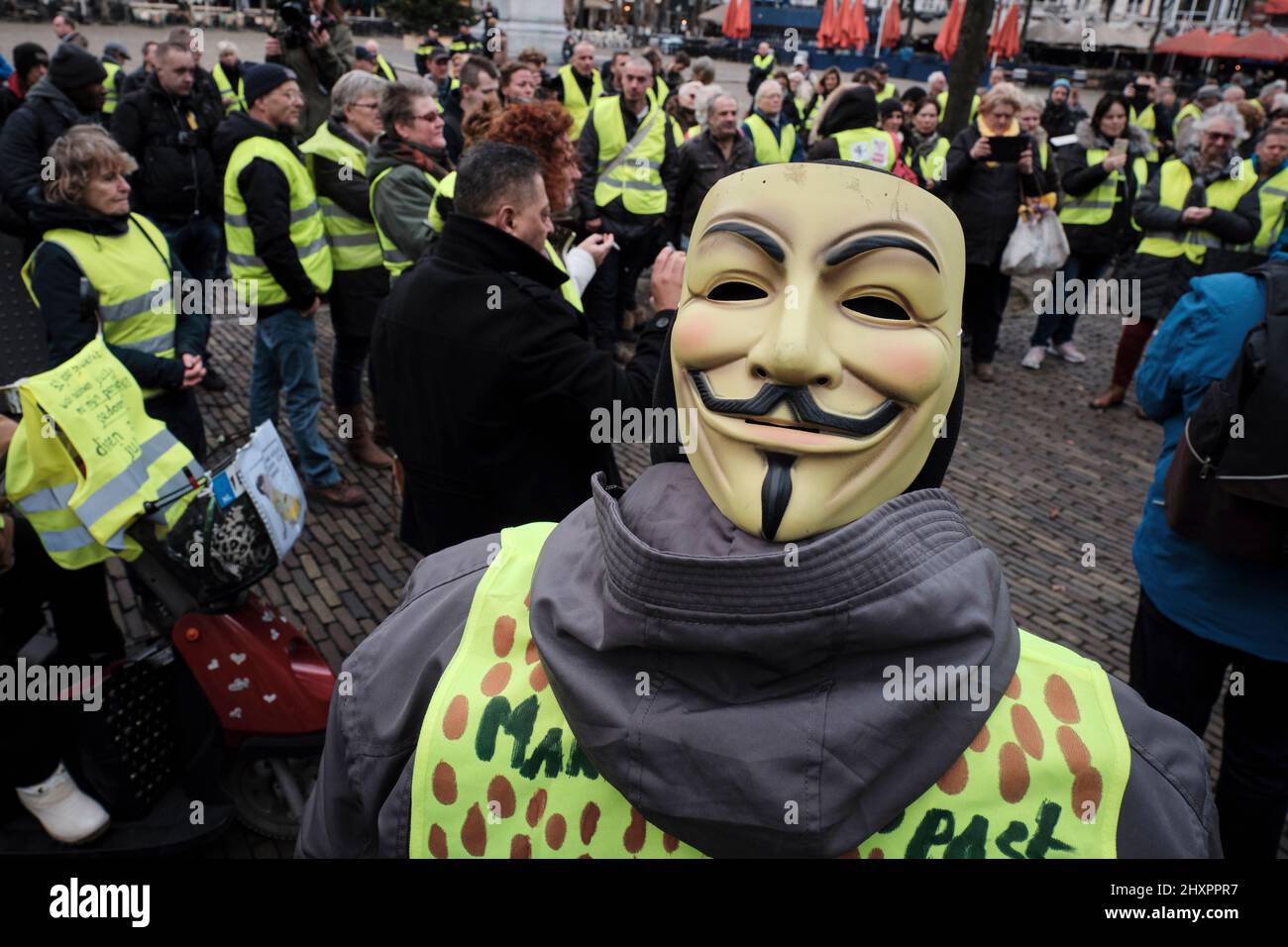 A member of the Yellow Vests; movement wears a mask of Anonymous; during the protest in front of parliament. Stock Photo