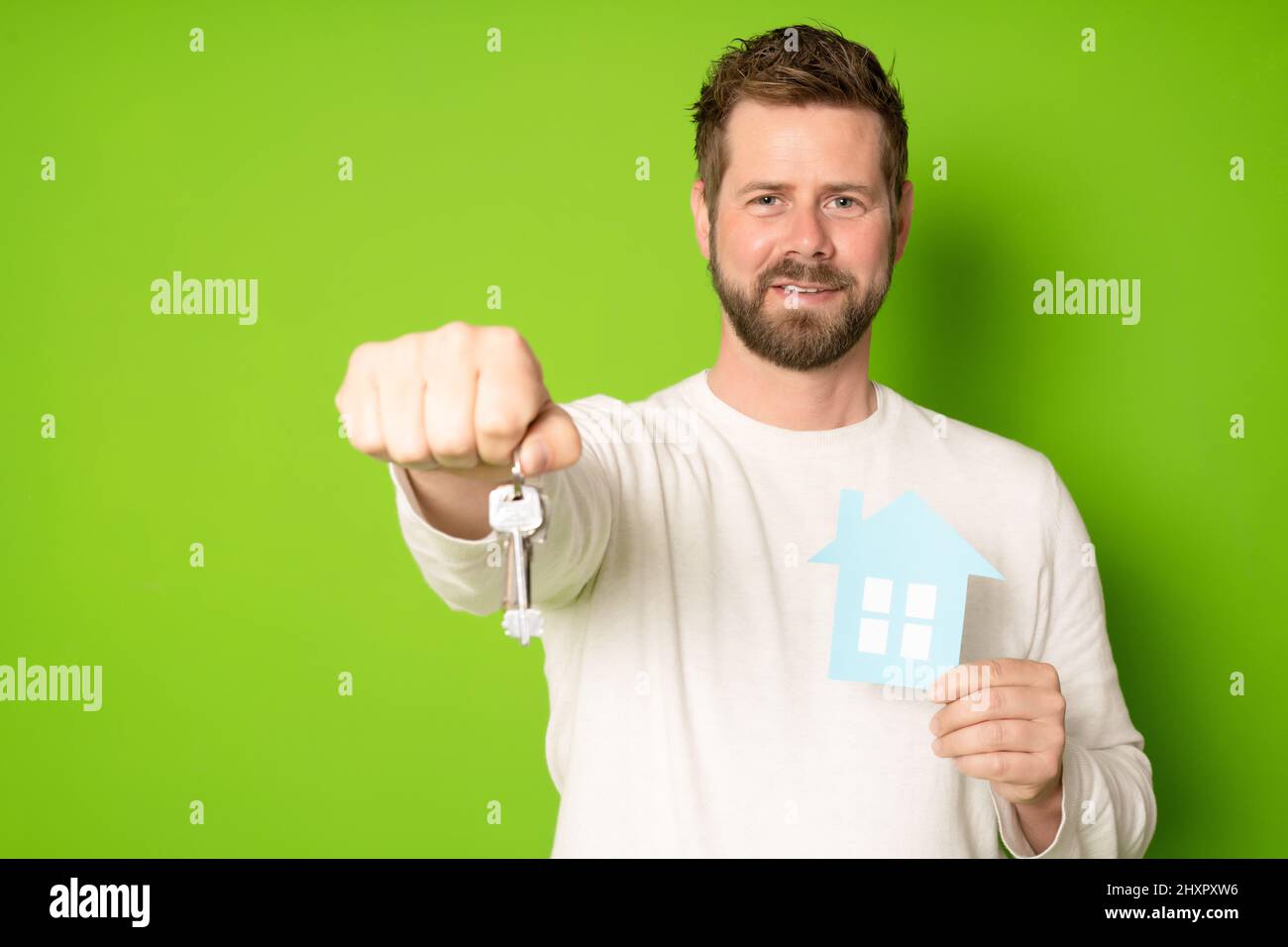Happy man holding a key and a model house isolated on green background ...