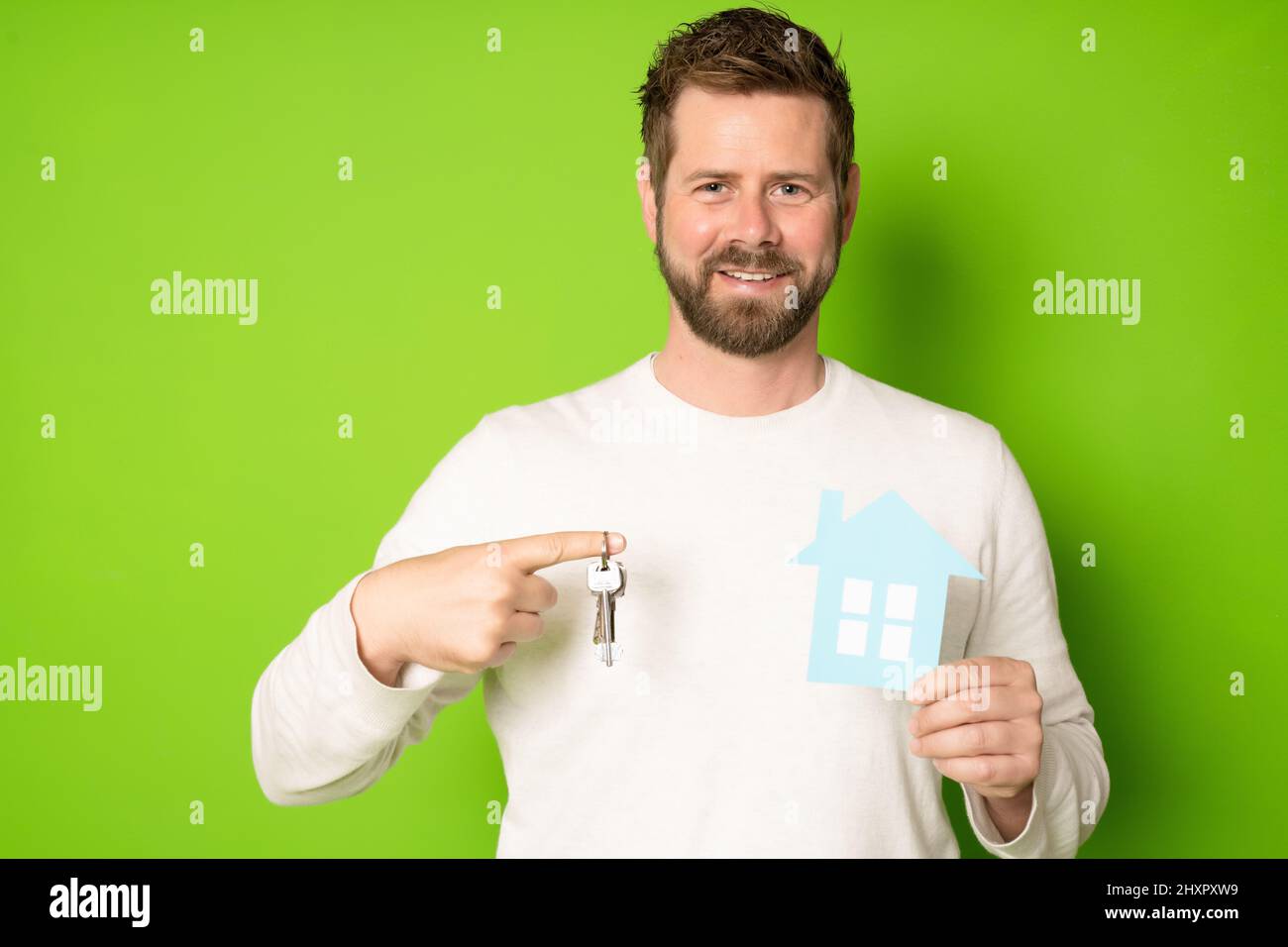 Happy man holding a key and a model house isolated on green background ...