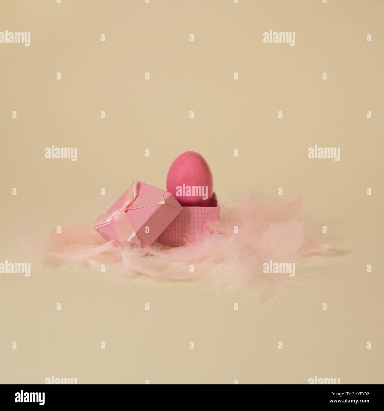 Bright pink Easter egg in gift box with feathers on yellow golden background Stock Photo