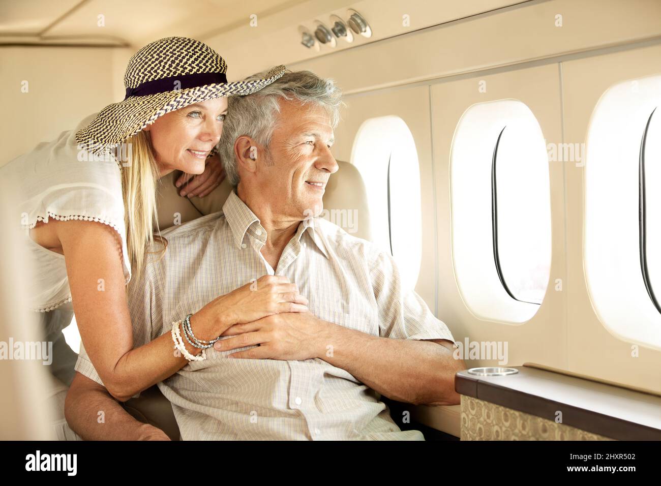 Taking a luxury trip. Smiling senior couple on an airplane looking out the window. Stock Photo