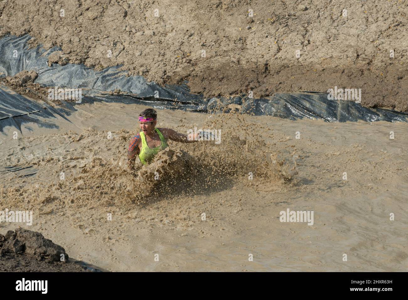 A female competitor slides into the mud pit of the Swampfoot Run with a muddy splash. Stock Photo