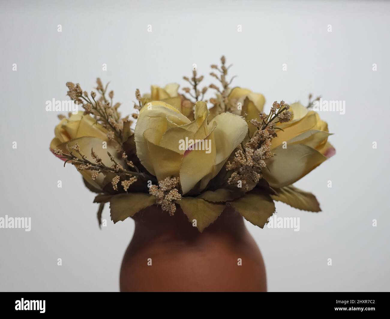 Artificial yellow roses in a clay vase against a white background Stock