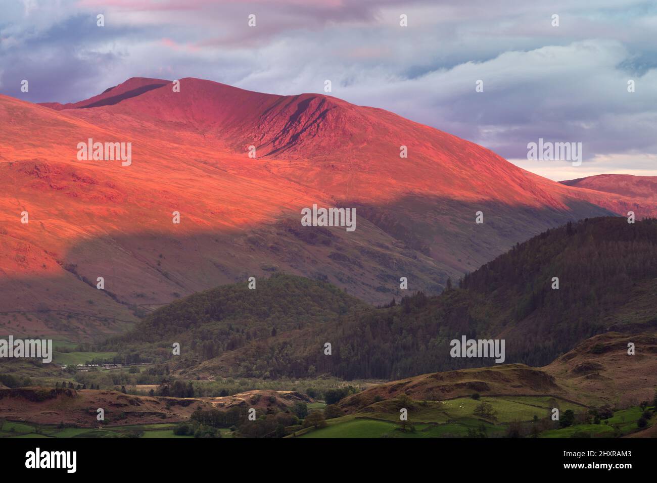 Evening light from the sunset casting a red glow and long shadows on Helvellyn mountain range in the English Lake District. Stock Photo
