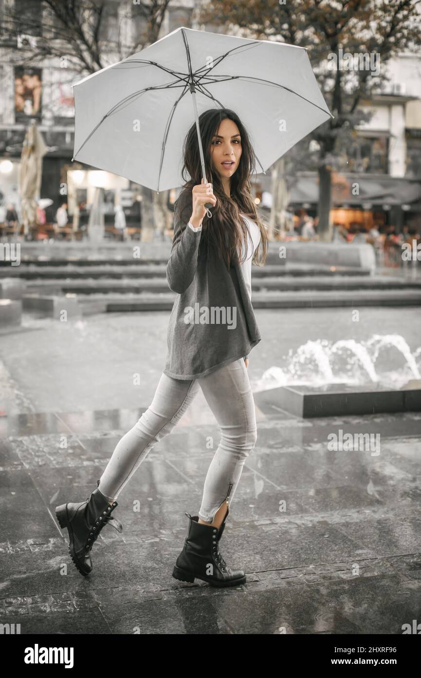 Portrait of young woman with an umbrella under rain on a city street ...