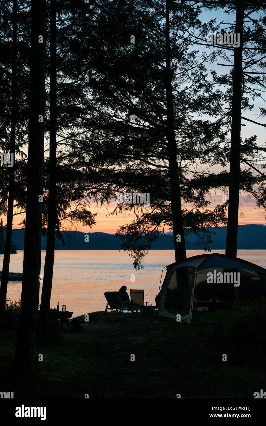 A tent and camp scene among trees overlooking water Stock Photo