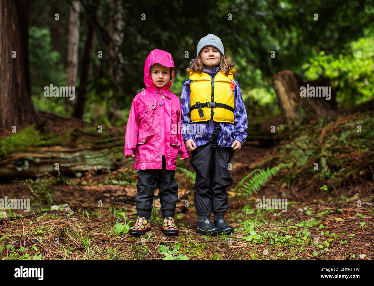 Two young girls in rain gear stand in a forest Stock Photo Alamy