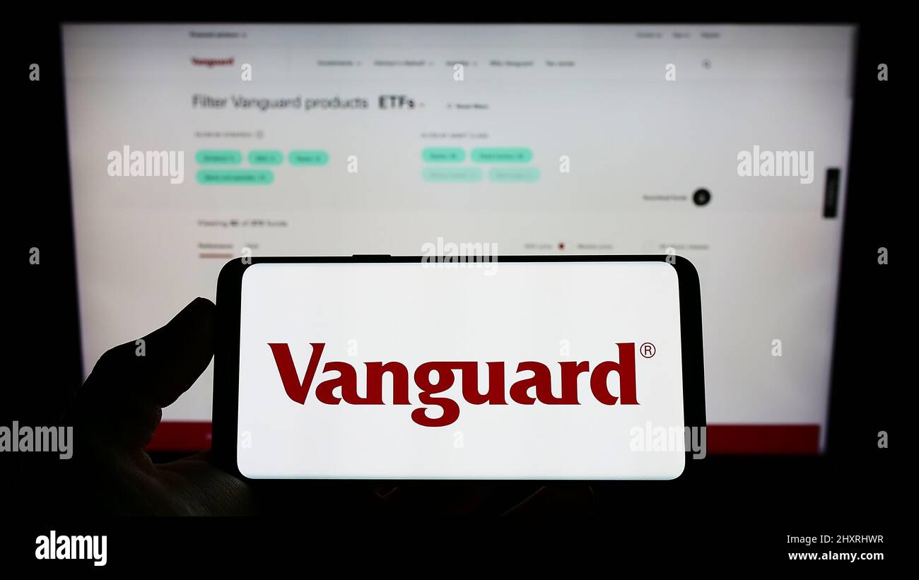 Person holding mobile phone with logo of American financial company The Vanguard Group Inc. on screen in front of webpage. Focus on phone display. Stock Photo
