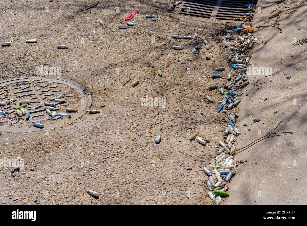 Multiple empty nitrous oxide canisters litter the street near a drain on Broadway Street near Tulane University in New Orleans, LA, USA Stock Photo