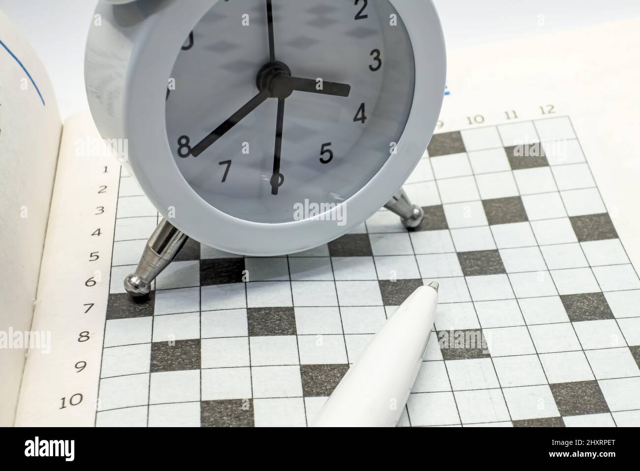 View of an alarm clock and a pen on the background of a crossword View of an alarm clock and a pen on the background of a crossword