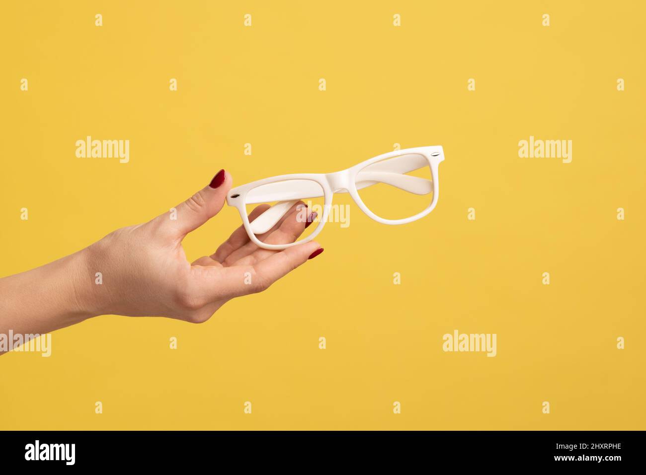 Profile side view closeup of woman hand holding and showing white eyeglasses frame. Indoor studio shot isolated on yellow background. Stock Photo