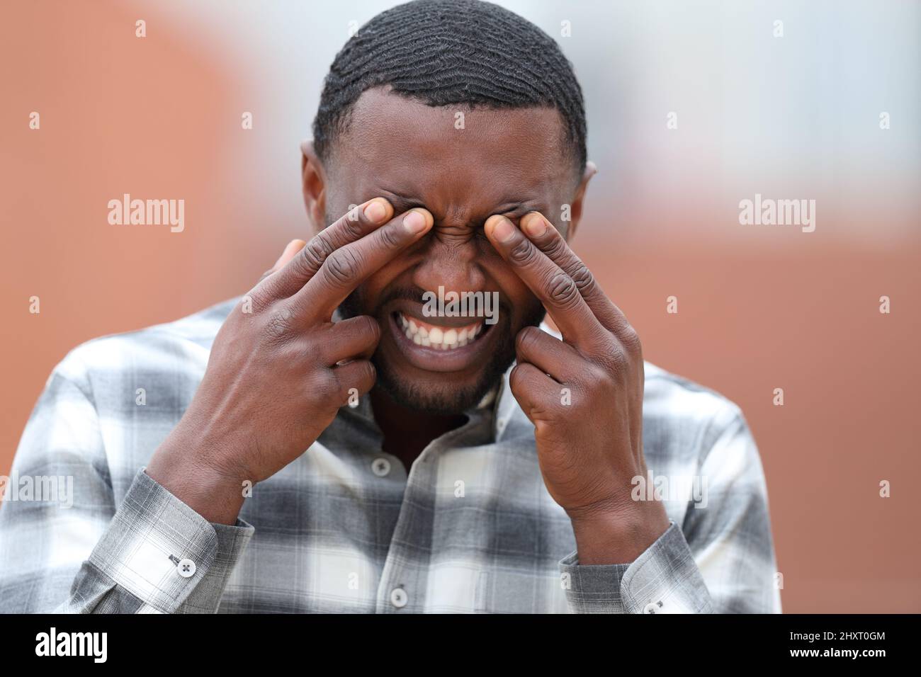 Front view portrait of a man with black skin scratching eyes in the street Stock Photo