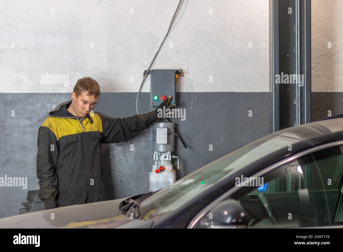 Hardworking man mechanic  lifting car standing at the service station. Stock Photo