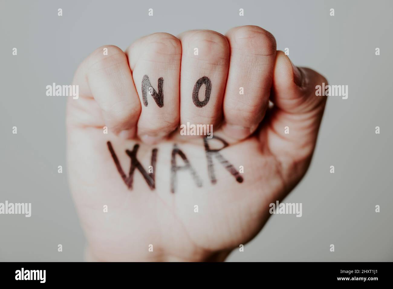 closeup of the raised fist of a man, with the text no war written in it, on a gray background Stock Photo