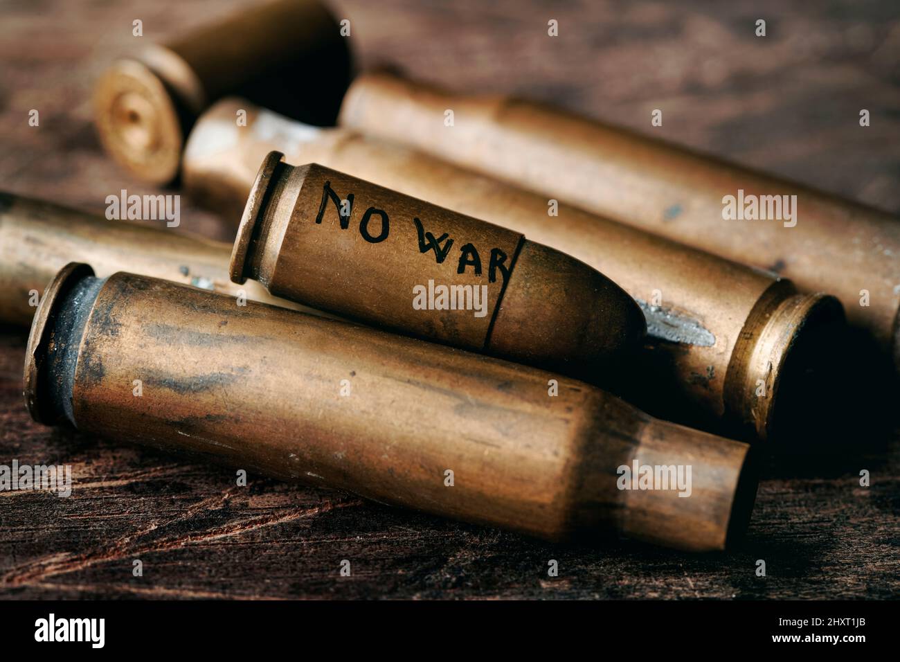 the text no war handwritten in a bullet on top of a bunch of used bullet shells, on a rustic surface Stock Photo