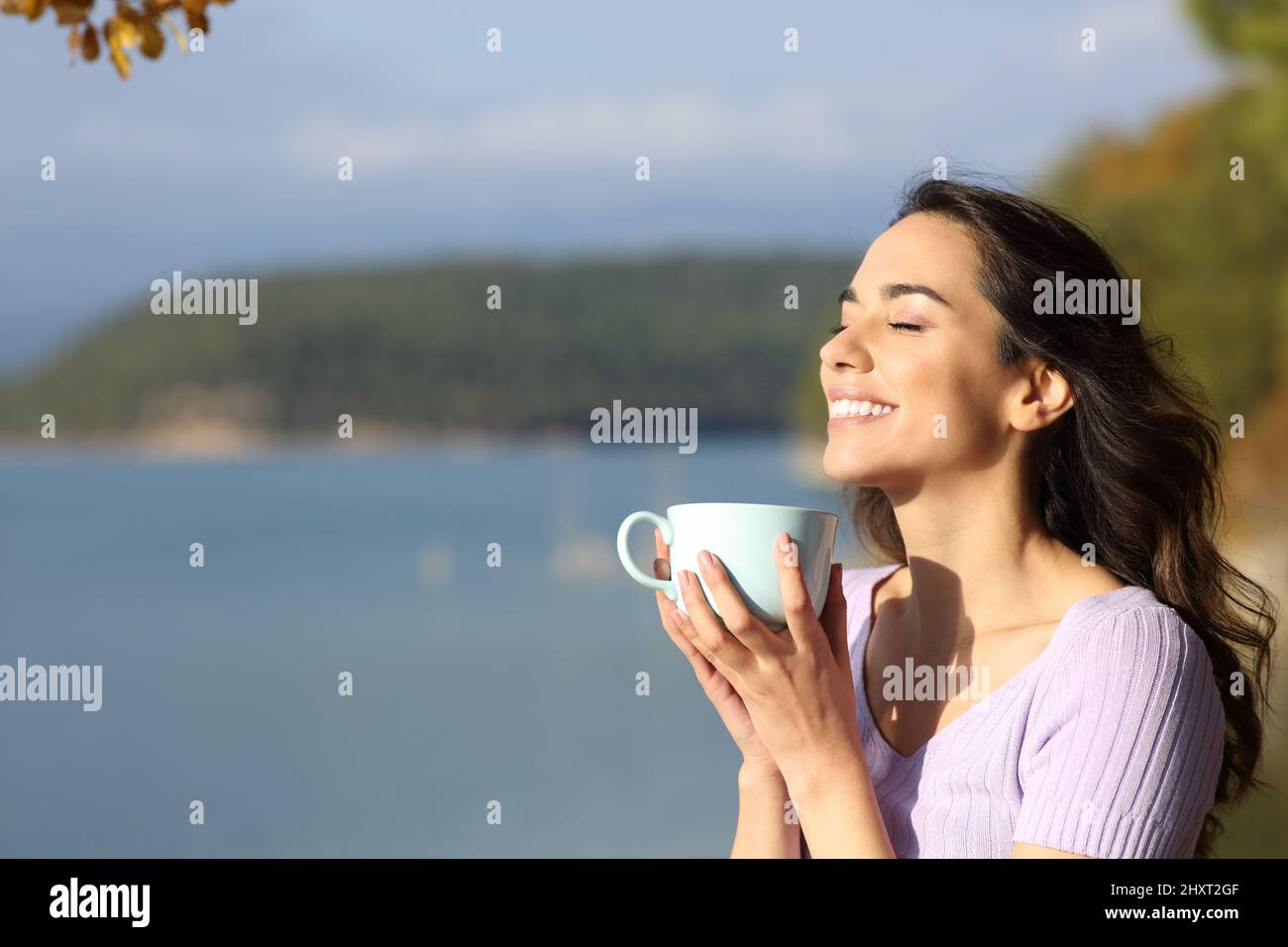 Happy woman laughing enjoying coffee mug standing in a beautiful lake Stock Photo